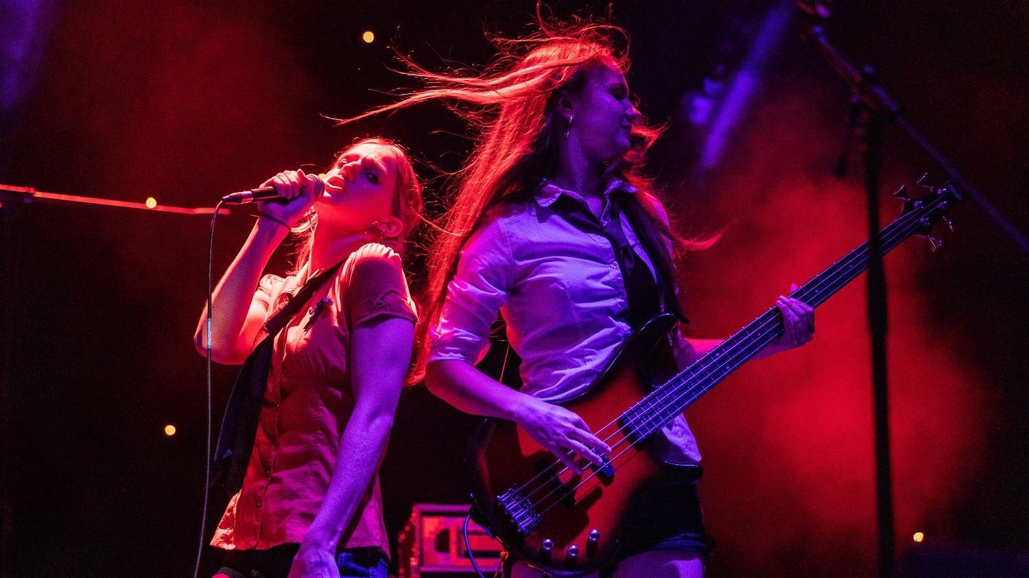 Two members of Soulstice perform on stage at Blackheath Halls. The person on the left is singing, and the person on the right is playing electric bass guitar.