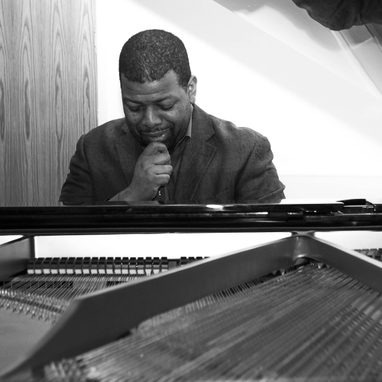 A man with dark hair and a beard is seated at a piano